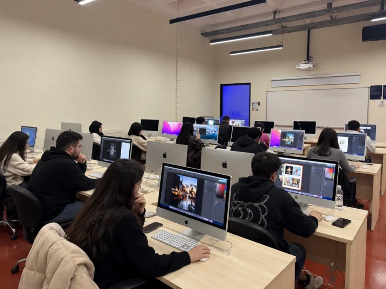 Farklı dijital görsel düzenleme uygulamalarını kullanan katılımcıların ve bilgisayar ekranlarının laboratuvarın sol tarafından çekilmiş geniş açılı görüntüsü.